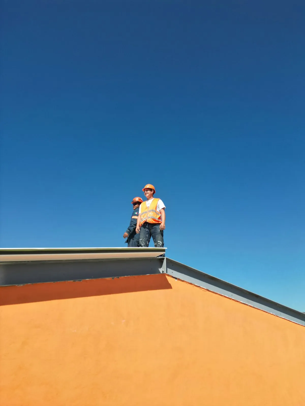 Twee dakdekkers met helm en veiligheidshesje op de rand van een plat dak