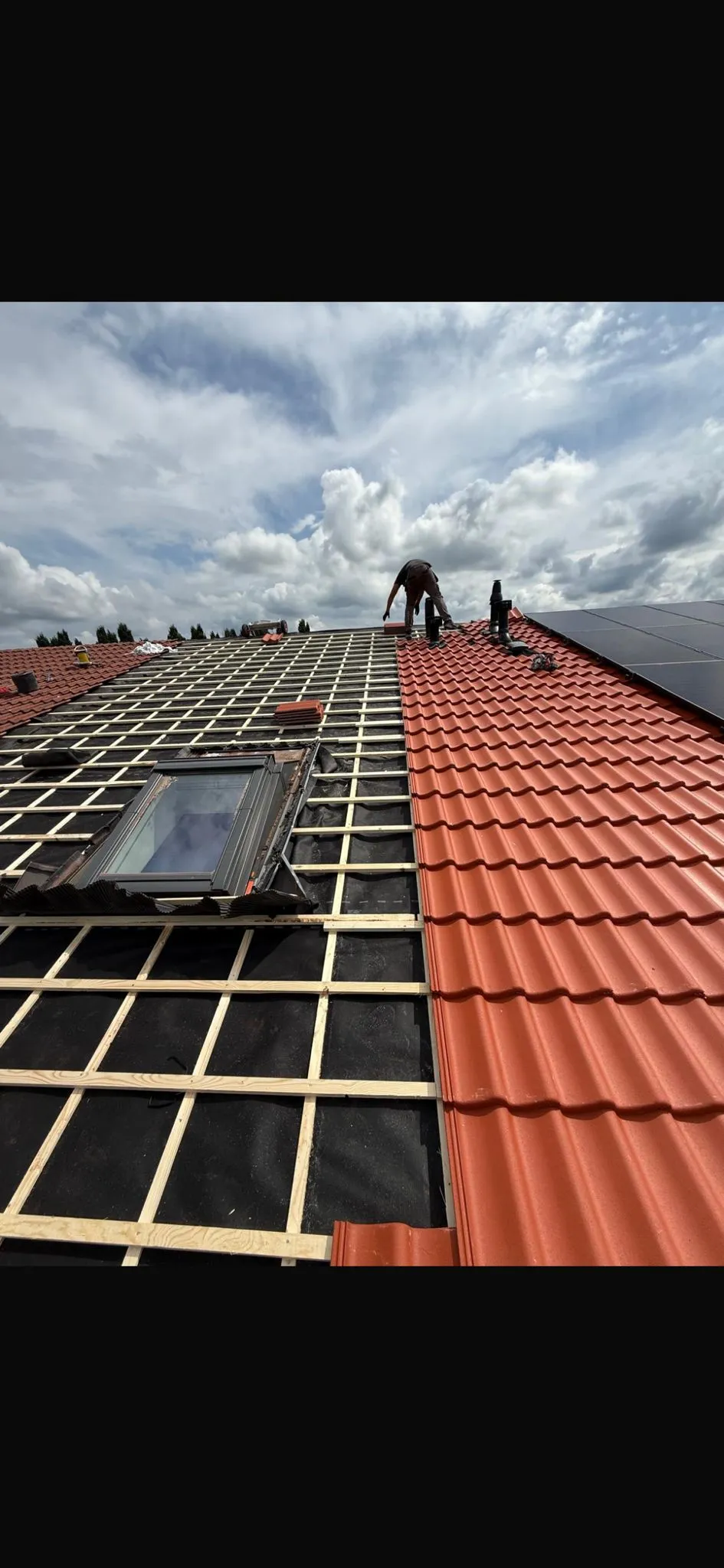 Dakdekker legt rode dakpannen op een nieuw pannendak met een dakraam en zonnepanelen op de aangrenzende kap