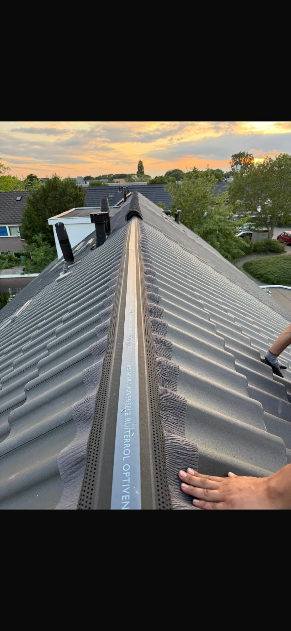Nok van een pannendak bij zonsondergang met een nieuw geplaatste ventilatierol onder de vorstpannen