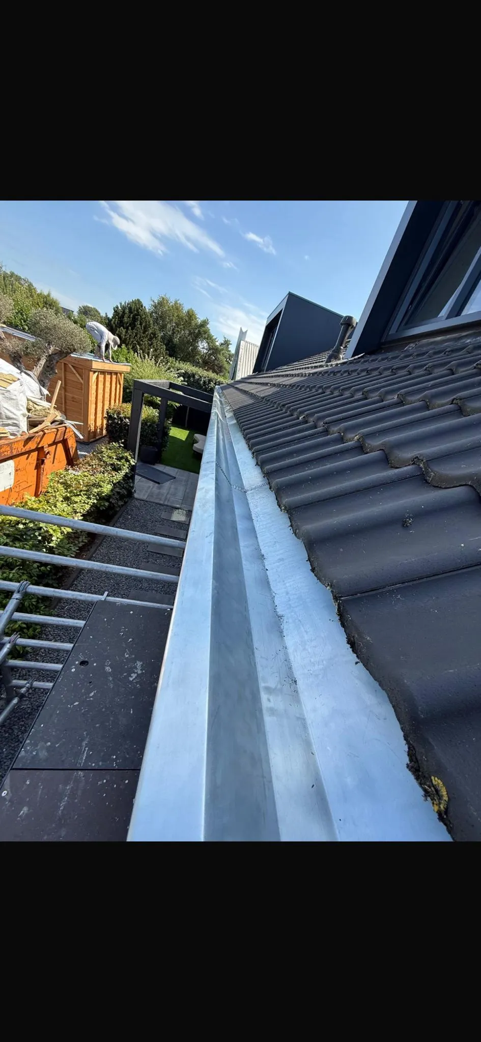 Nieuwe zinken dakgoot langs een pannendak op een bouwlocatie