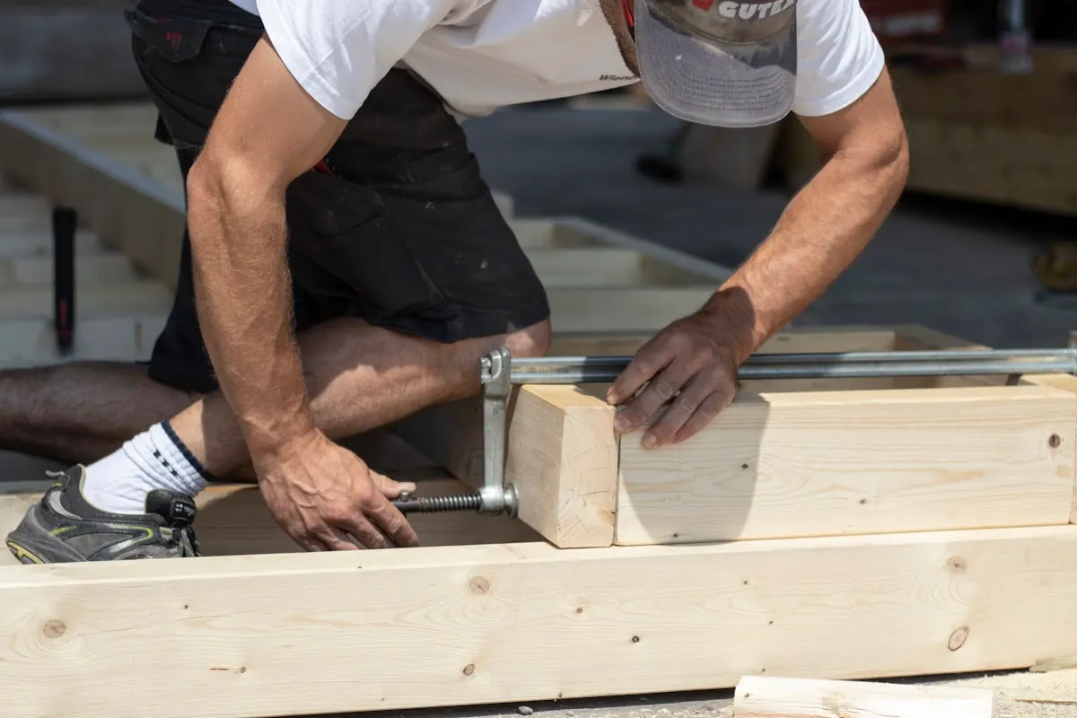 Dakdekker zet met een klem twee houten balken vast tijdens het werk aan een dakconstructie