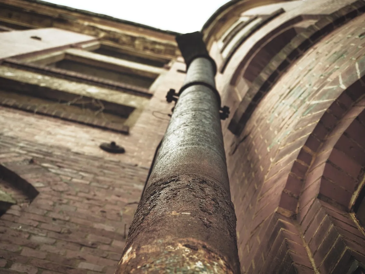 Zinken regenpijp langs een bakstenen gevel, van onderaf gefotografeerd